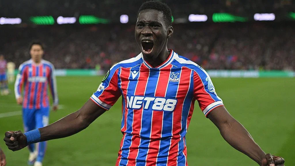 Ismaila Sarr celebrates in Crystal Palace's red and white striped shirt, with his fists clenched and held out by his side and his mouth open in happiness